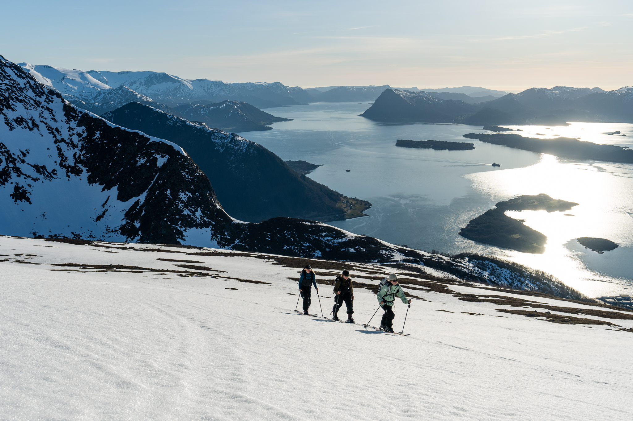 3 women on skis skin up a mountain on an island